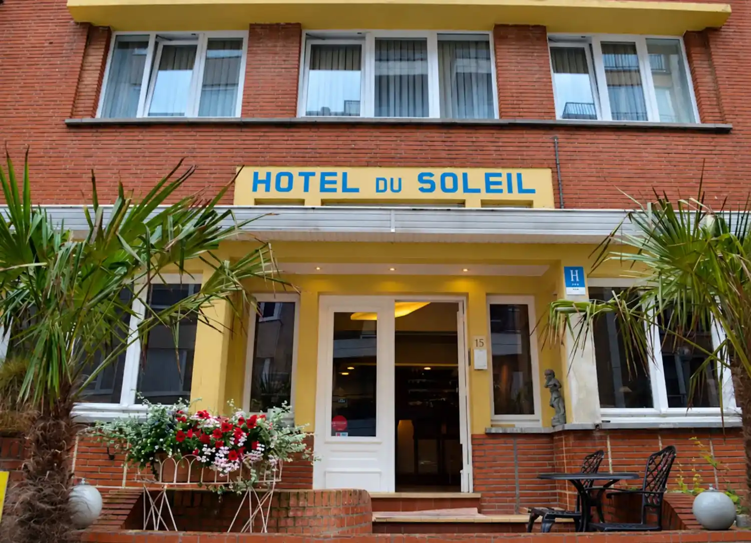 Ingang van Hotel du Soleil met het gele uithangbord, planten en bloemen