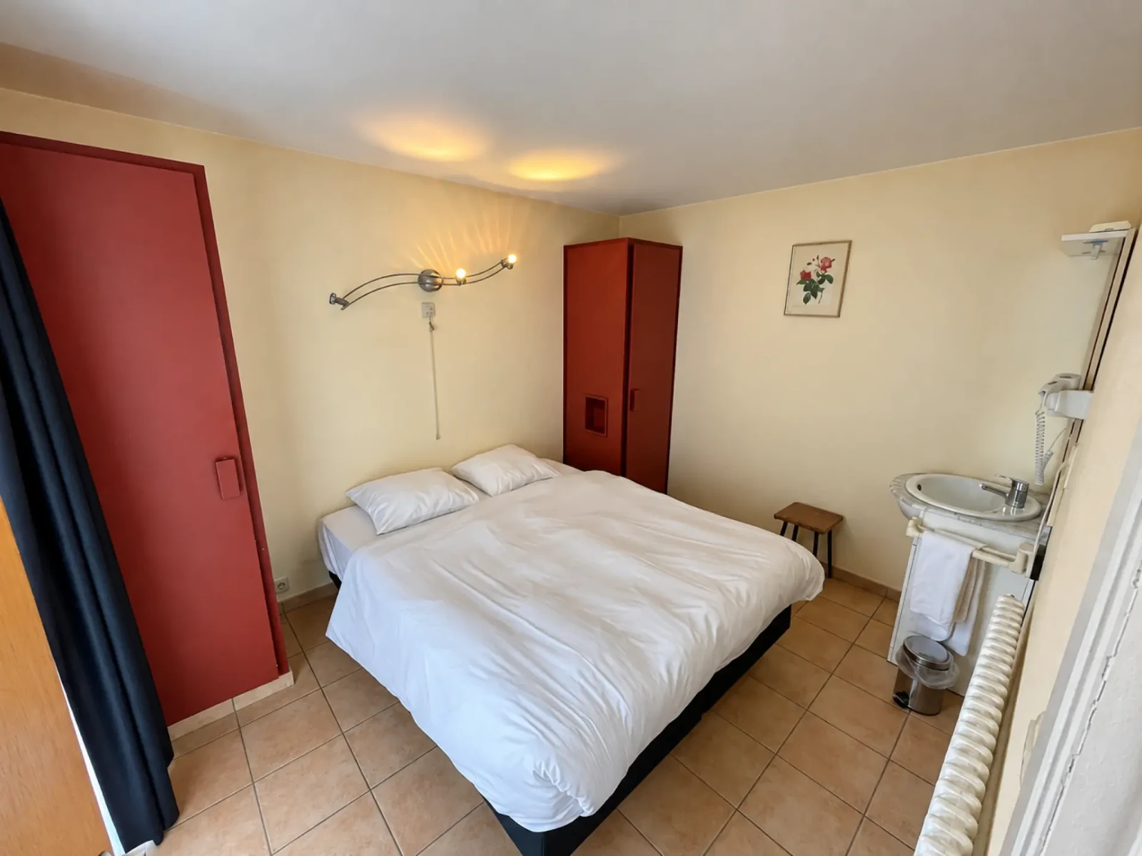 Slaapkamer met wit beddengoed, rode kasten en een wastafel